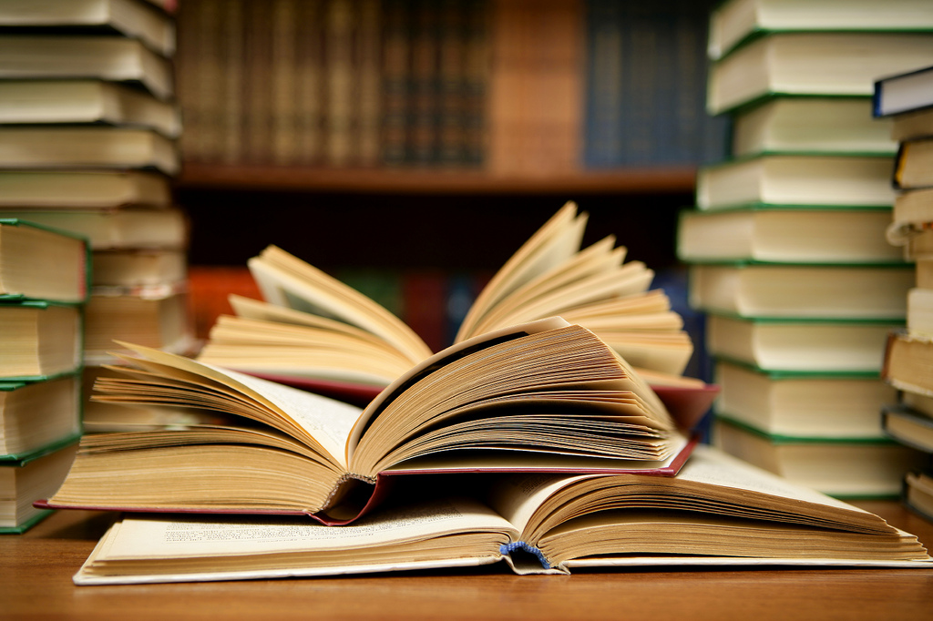 Lots of books for on a desk and on shelves in the background
