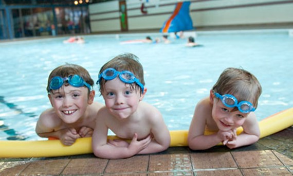 3 boys with goggles on top of head at the edge of the swimming pool