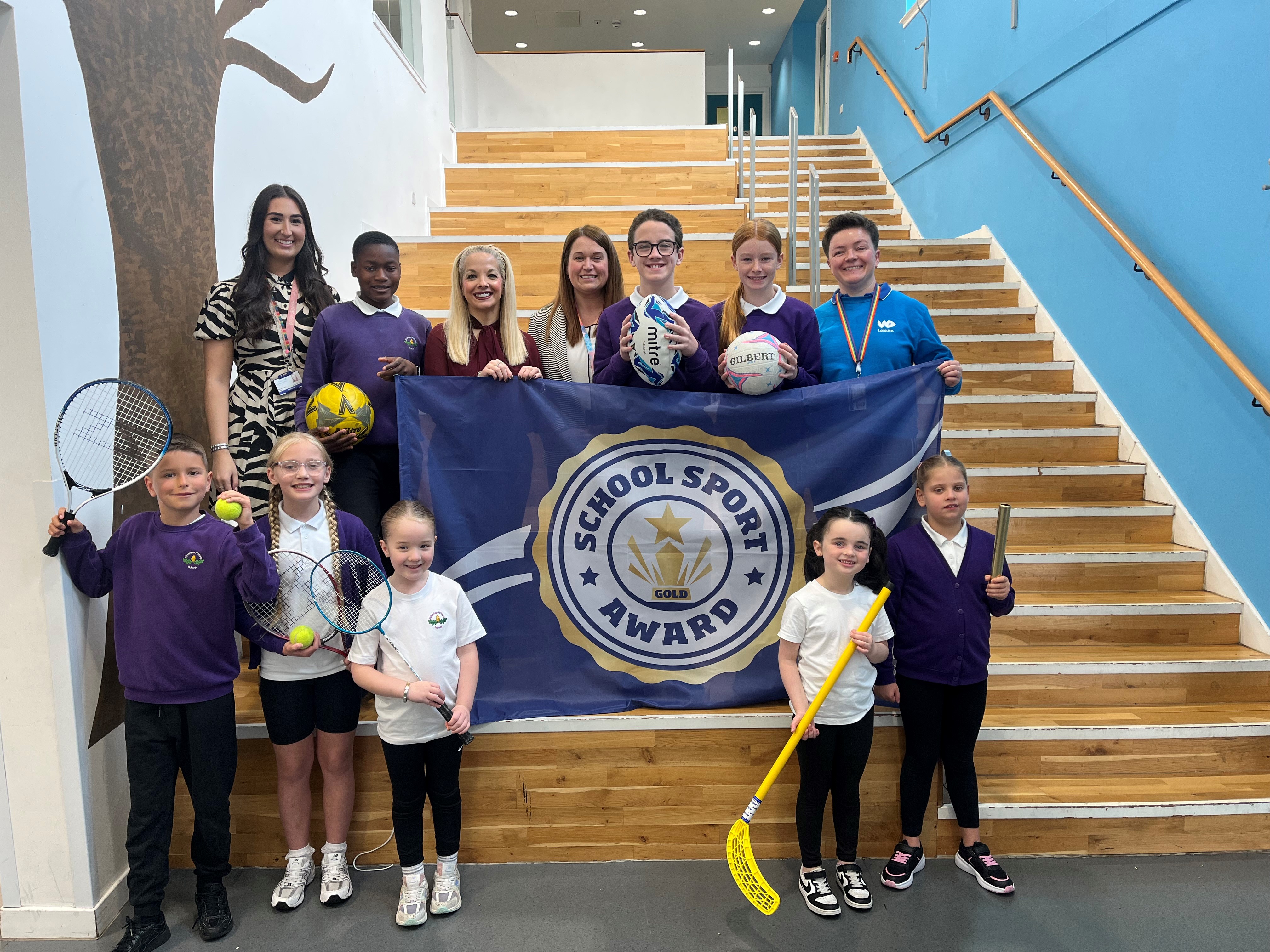 Education Convener Councillor Clare Steel with Aitkenbar Primary School pupils and staff holding the Gold School Sport Award banner.