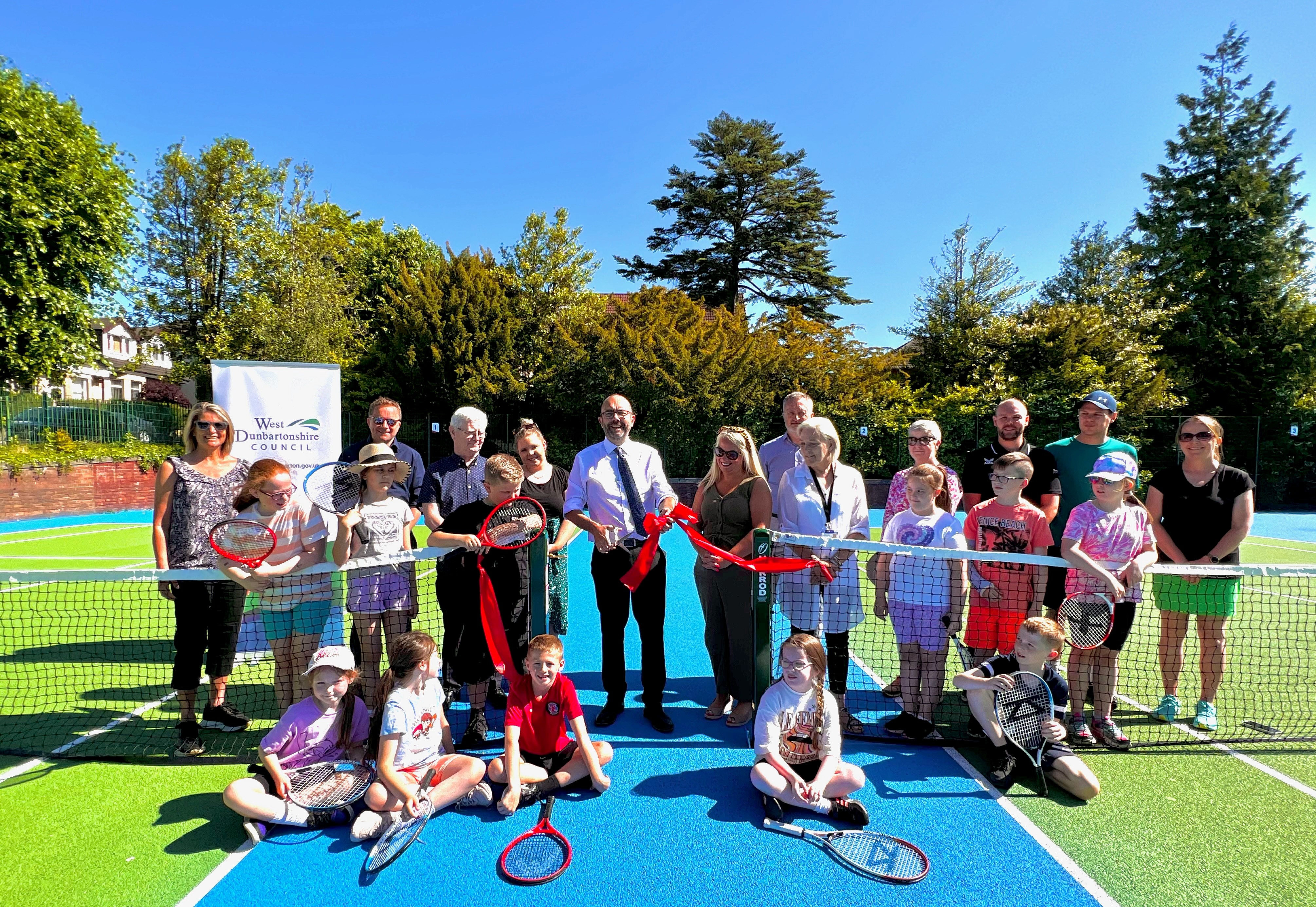 Councillors, Members of WDL and tennis association with children from Whitecrook Primary school cut red ribbon on tennis courts in Whitecrook