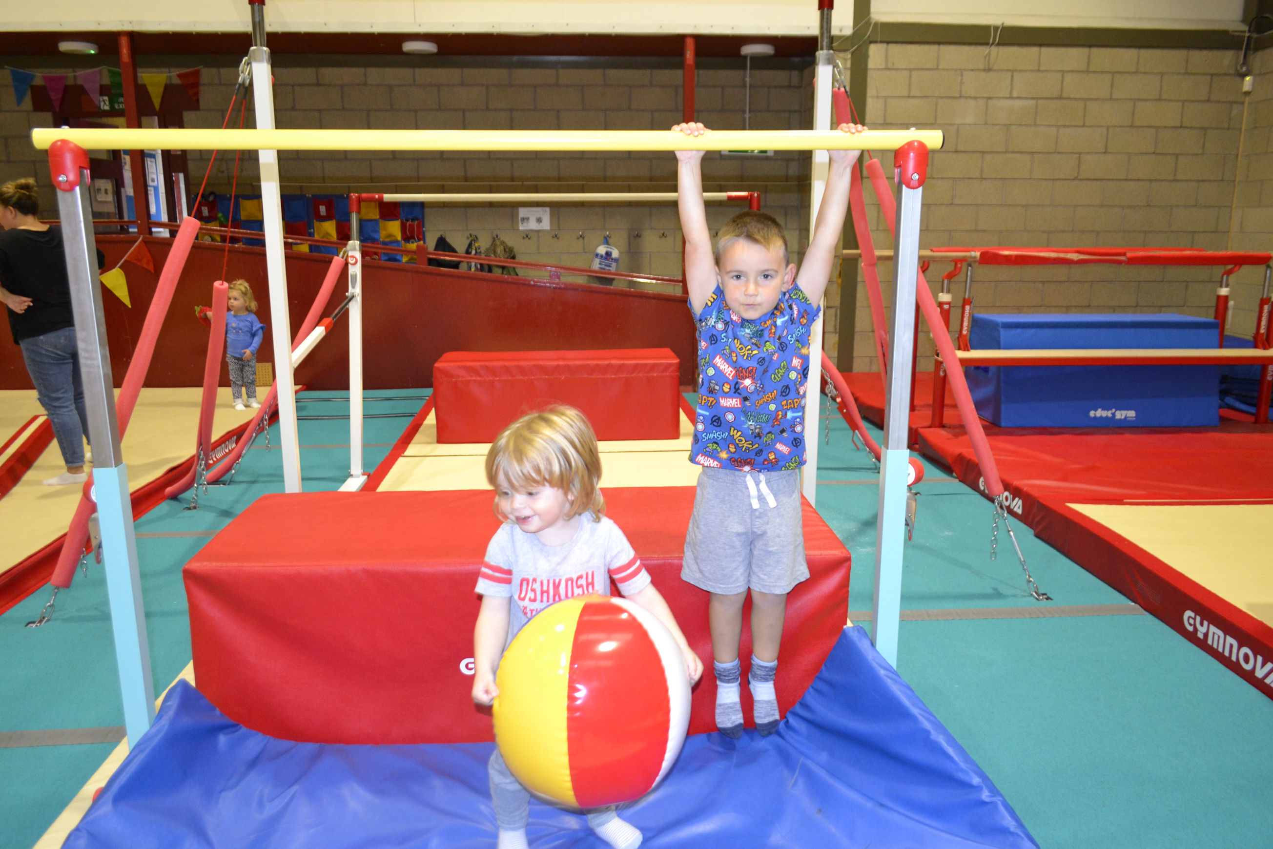 image of Gymnastics - boy hanging on low bar and another with a beach ball