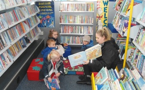 Woman reading a story to 3 children in the mobile library