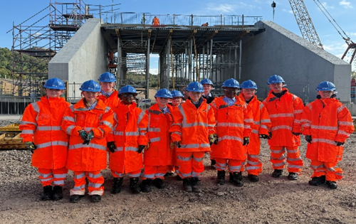 A panoramic view of the Exxon Bowling site showing construction activity and machinery, with pupils observing safely from a distance.
