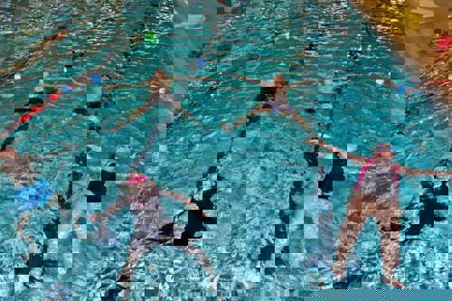 5 young people floating in star shape in the swimming pool