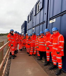 A construction worker in high-vis safety gear explaining the bridge structure to a group of pupils on the site tour.